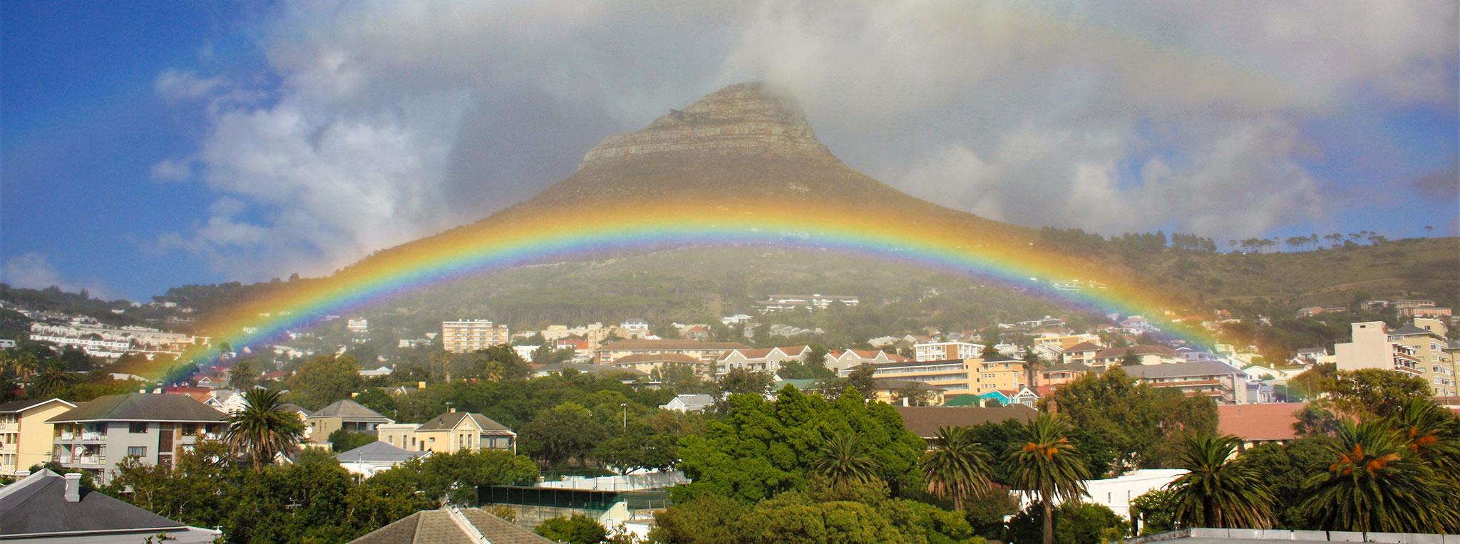 Vivid rainbow arching across Lion's Head mountain over the Cape Town suburbs.