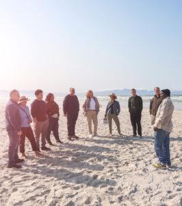 Small group of guests in a circle listening to their guide at Muizenberg beach.