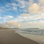 Vast , empty sandy beach with calm waves at sunset.
