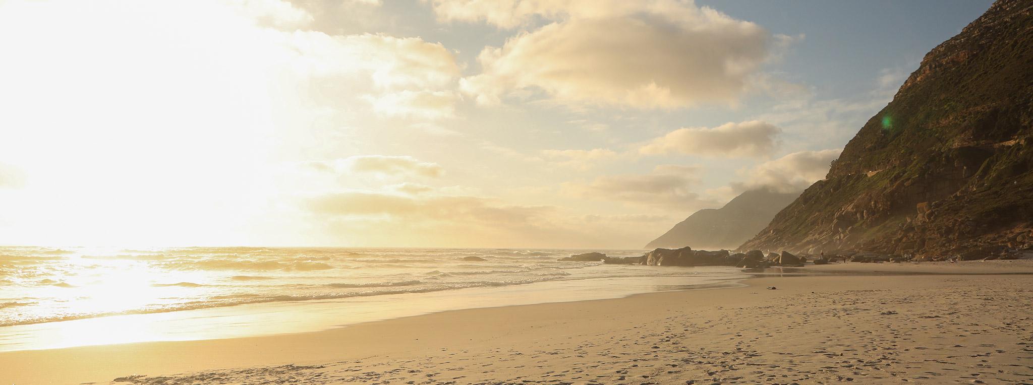 The sun sets in the ocean infront of Noordhoek beach leaving a golden light on the sand.