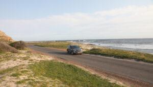 A rental vehicle used on different types of self-drive tours in South Africa drives along a tarmac road on the coast in the Western Cape.