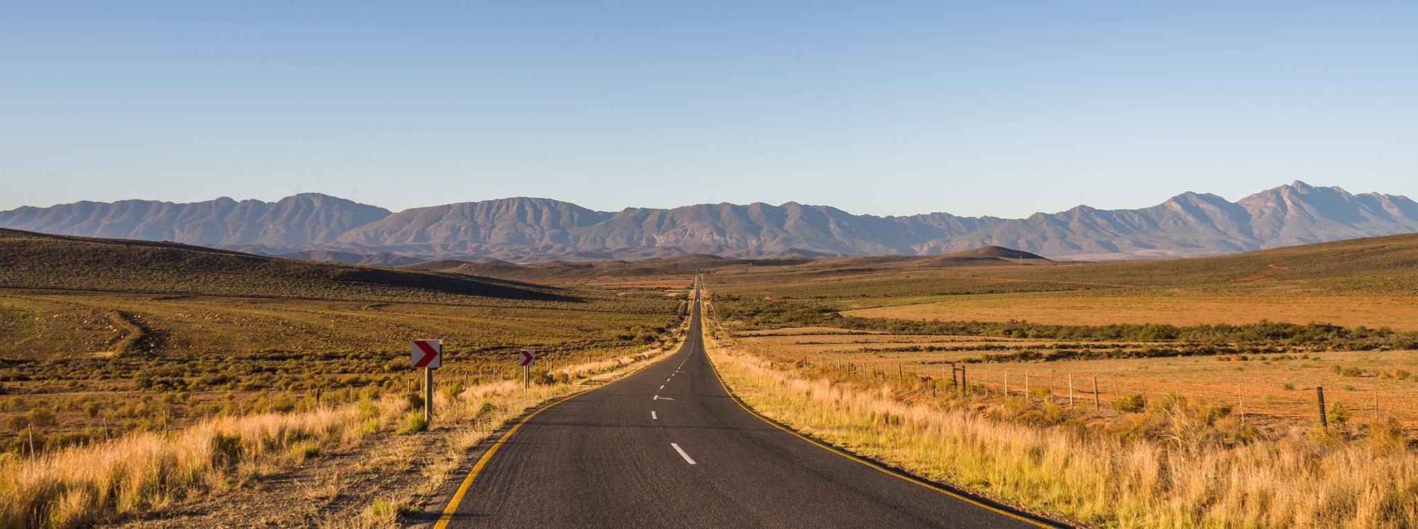 Long straight tarmac road stretching toward distant mountains on Route 62, South Africa.