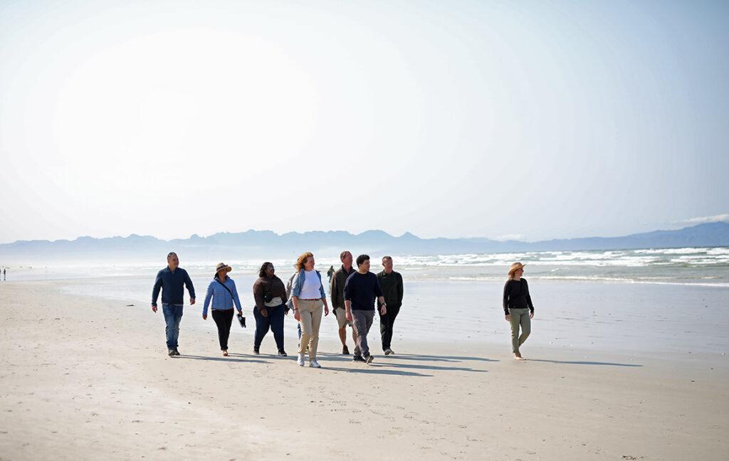 A small group of travellers on a guided tour walking along Muizenberg Beach.