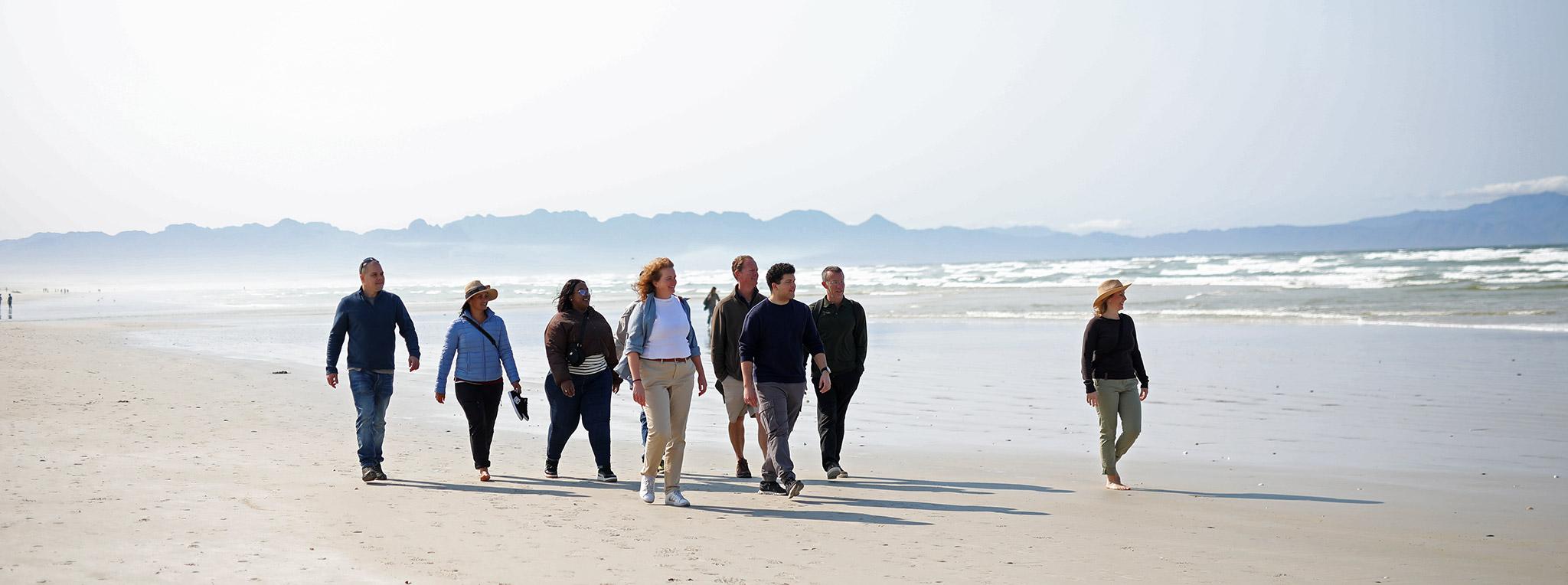 A small group of travellers on a guided tour walking along Muizenberg Beach.