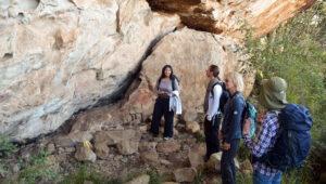 A guide explaining ancient San rock art to a small group of guests at a sandstone cave.
