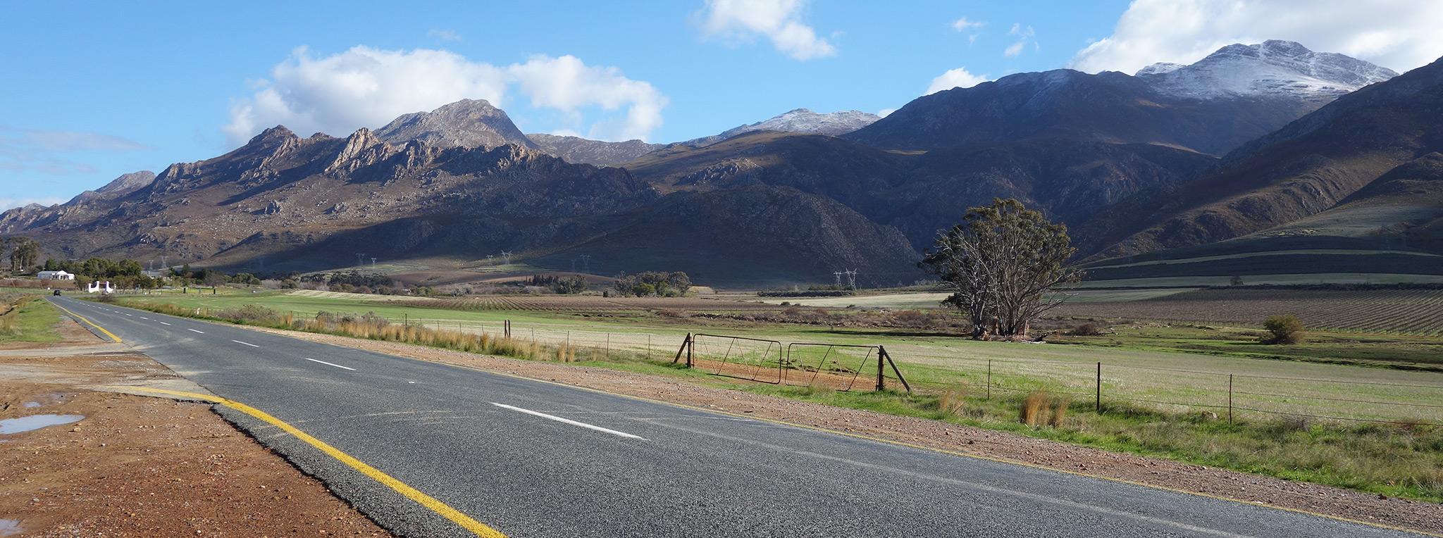 A road through the Western Cape farmlands with dramatic mountains in the background, South Africa.