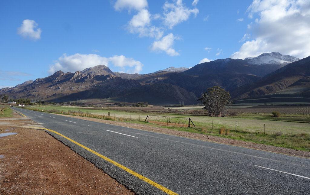 A road through the Western Cape farmlands with dramatic mountains in the background, South Africa.