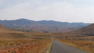 A straight road stretching towards the Drakensberg mountain range across open grasslands.