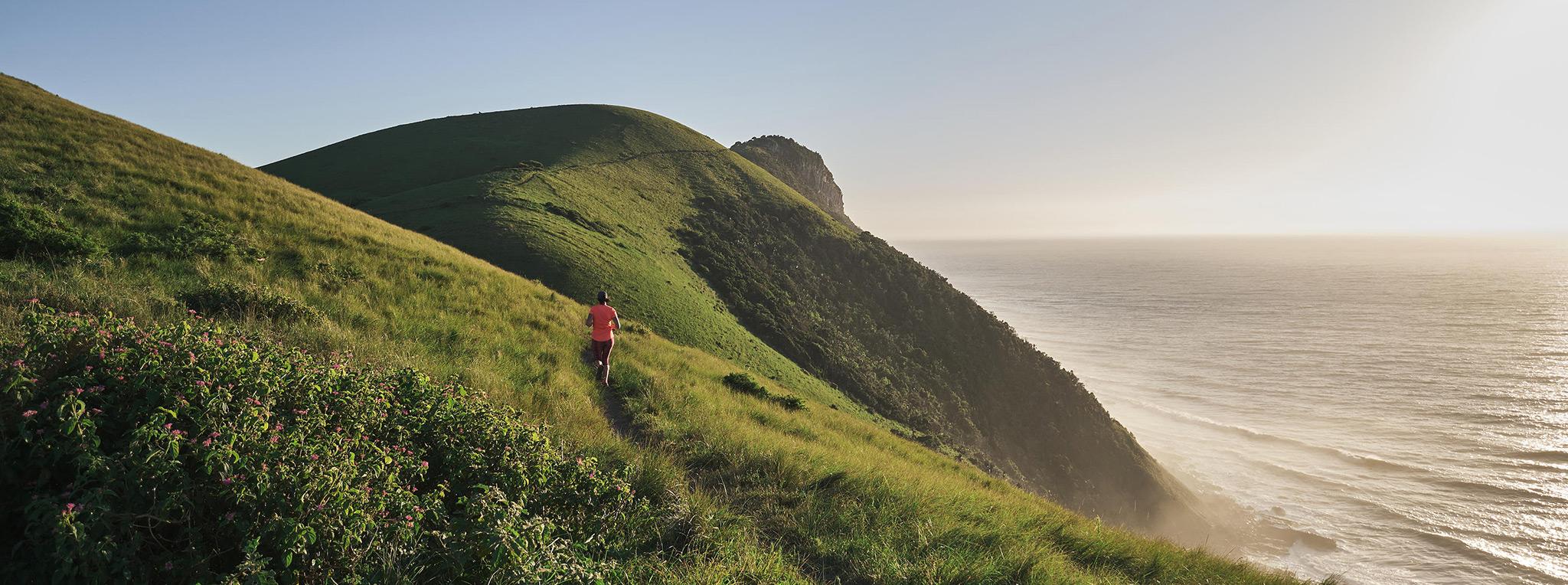 Person walking along a Wild Coast hiking trail on the green hills of South Africa's coast, near Umngazi Lodge.