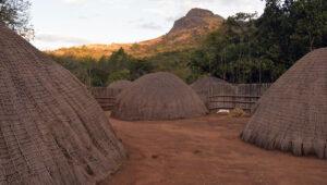 Traditional domed Swazi beehive huts in a cultural village with mountains in the background.
