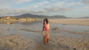Two women walking on the wide, empty sands of Noordhoek Beach with mountains in the background, Cape Town.