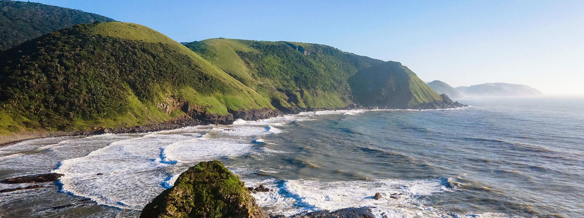 Rugged coastline with crashing waves and green hills along the Wild Coast South Africa.