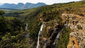 Waterfall cascading into a forested gorge with rolling Drakensberg mountains in the background.