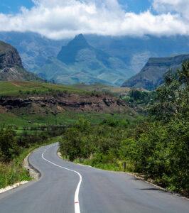 Winding road cutting through lush green valleys towards the dramatic peaks of Royal Natal National Park.