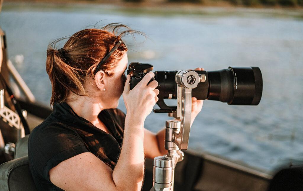 Woman on a photography boat safari capturing wildlife in the distance.