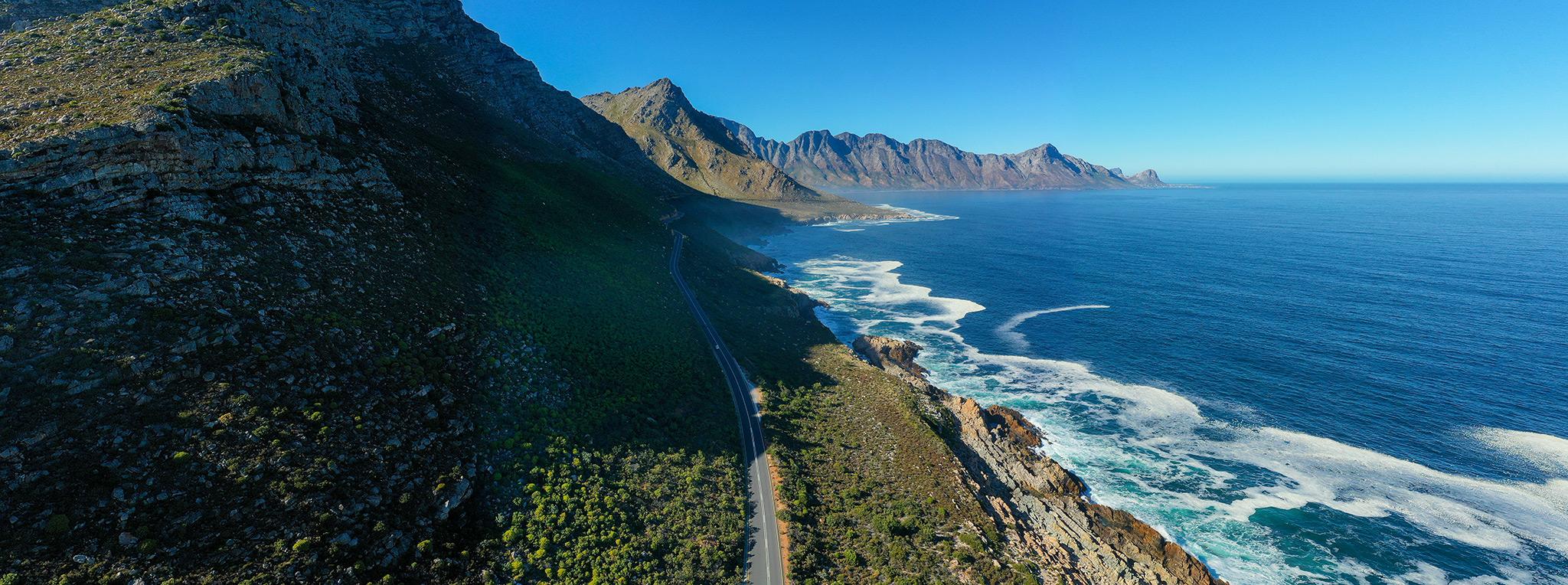 Aerial view of a long straight road between mounatins and the ocean, part of the Garden Route.