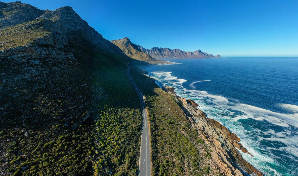Aerial view of a long straight road between mounatins and the ocean, part of the Garden Route.