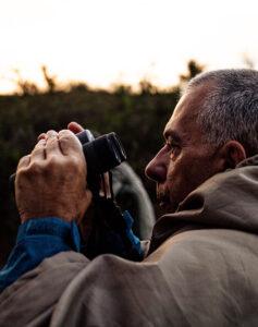 Guest holding binoculars to observe wildlife while on a game drive at sunset.