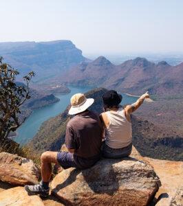 Two guests sit at the top of Blyde River Canyon pointing towards the landscape.
