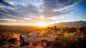 Oudtshoorn safari at sunset: people in a jeep watch the sun set over the mountains.