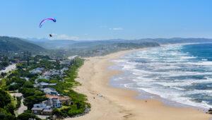 A person paragliding over the vaste white sandy beach of wilderness.