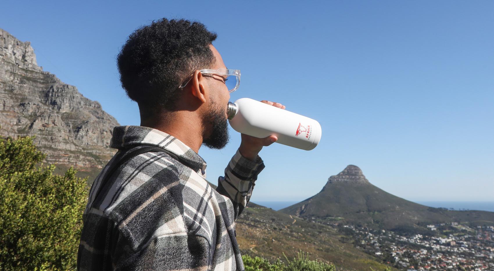 Man drinking from a white reusable water bottle with a view of Table Mountain in Cape Town. Man drinking from a white reusable water bottle with a view of Table Mountain in Cape Town.