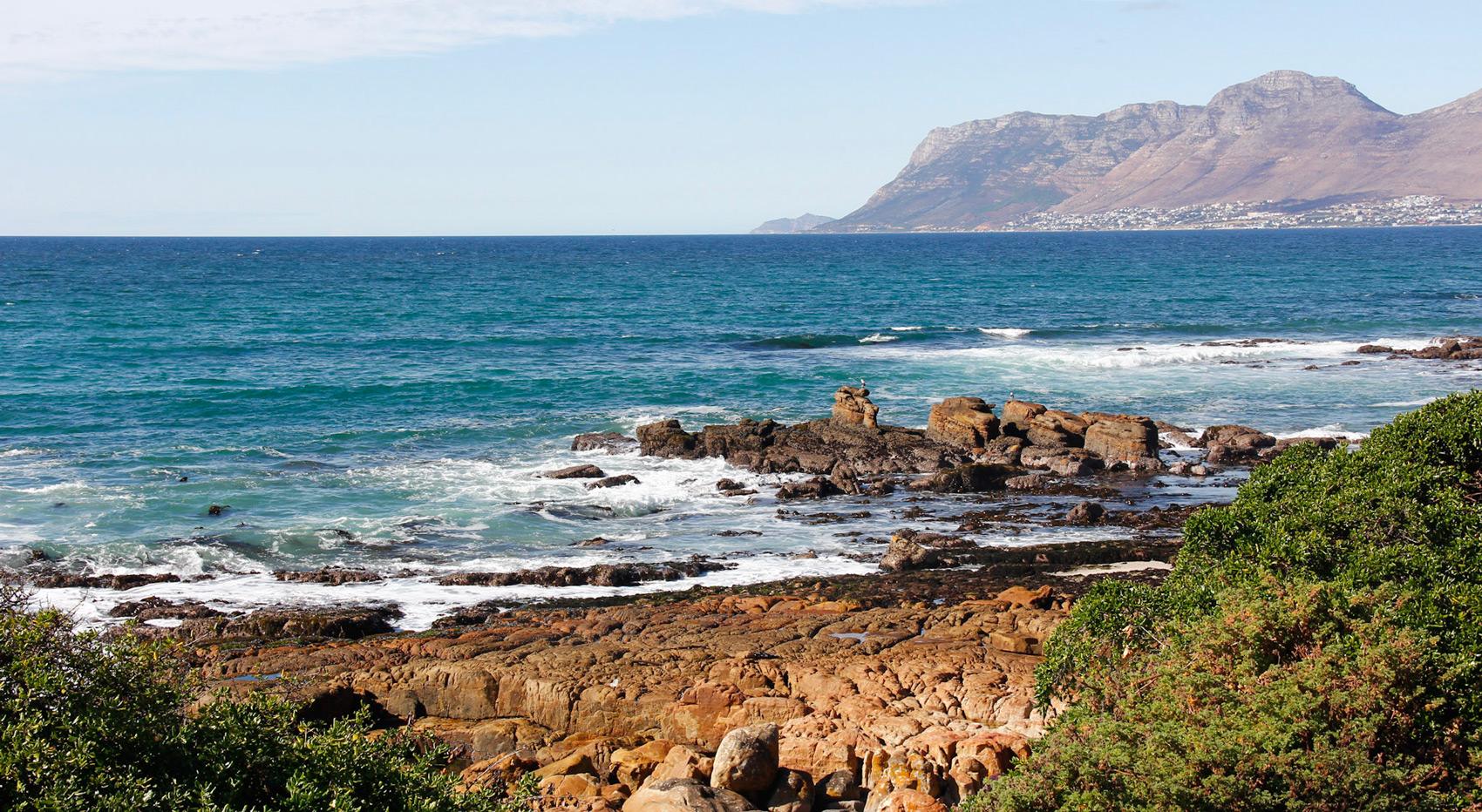 Rocky coastline with turquoise ocean waves crashing, overlooking a mountain in Cape Town, South Africa. Rocky coastline with turquoise ocean waves crashing, overlooking a mountain in Cape Town, South Africa.
