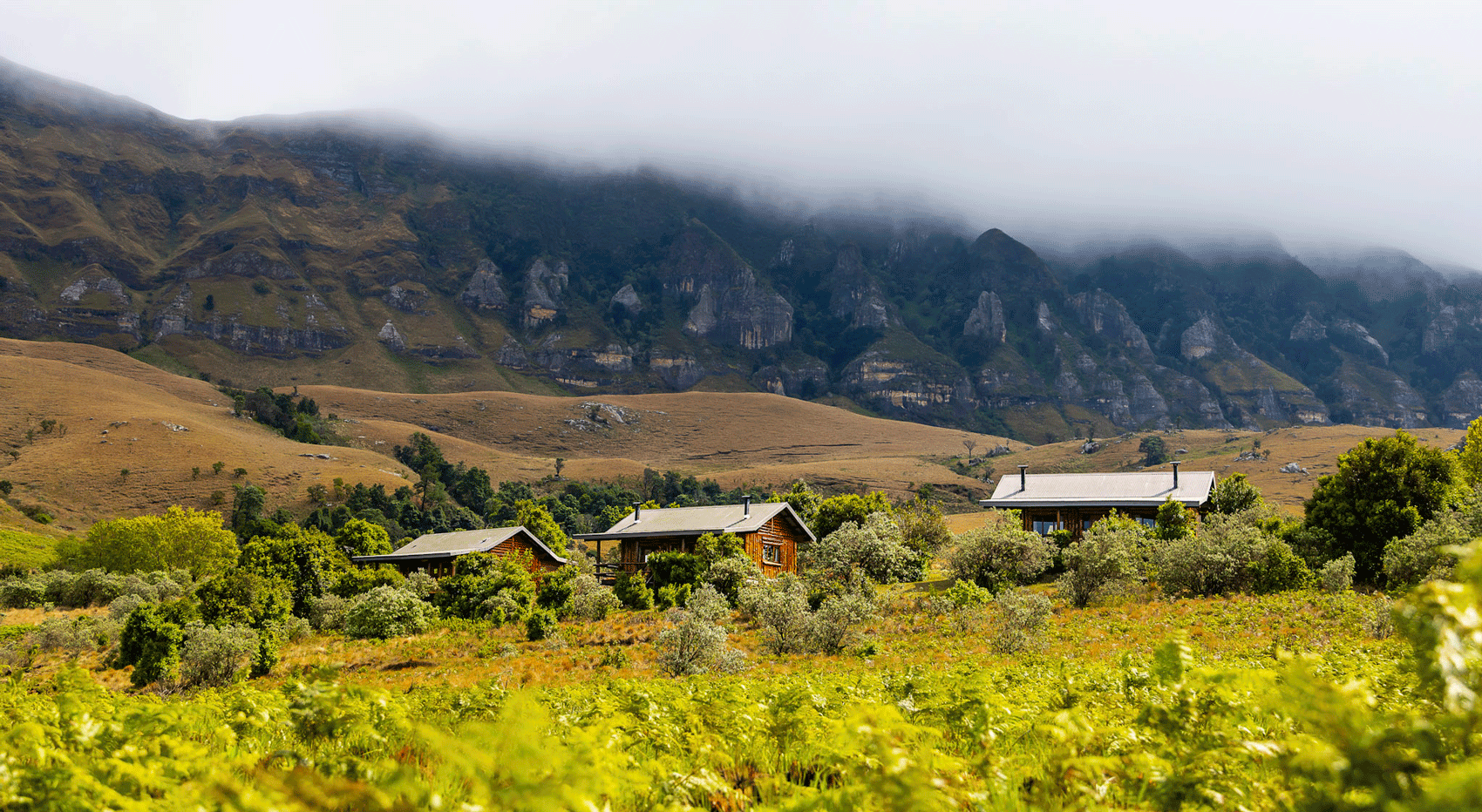 Cozy cabins nestled in a lush valley with dramatic, misty mountains in South Africa. Cozy cabins nestled in a lush valley with dramatic, misty mountains in South Africa.